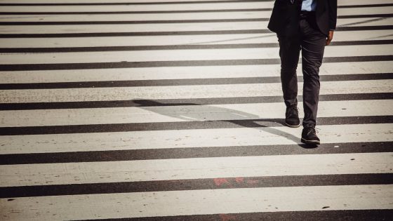 faceless businessman with smartphone walking on crosswalk in sunlight
