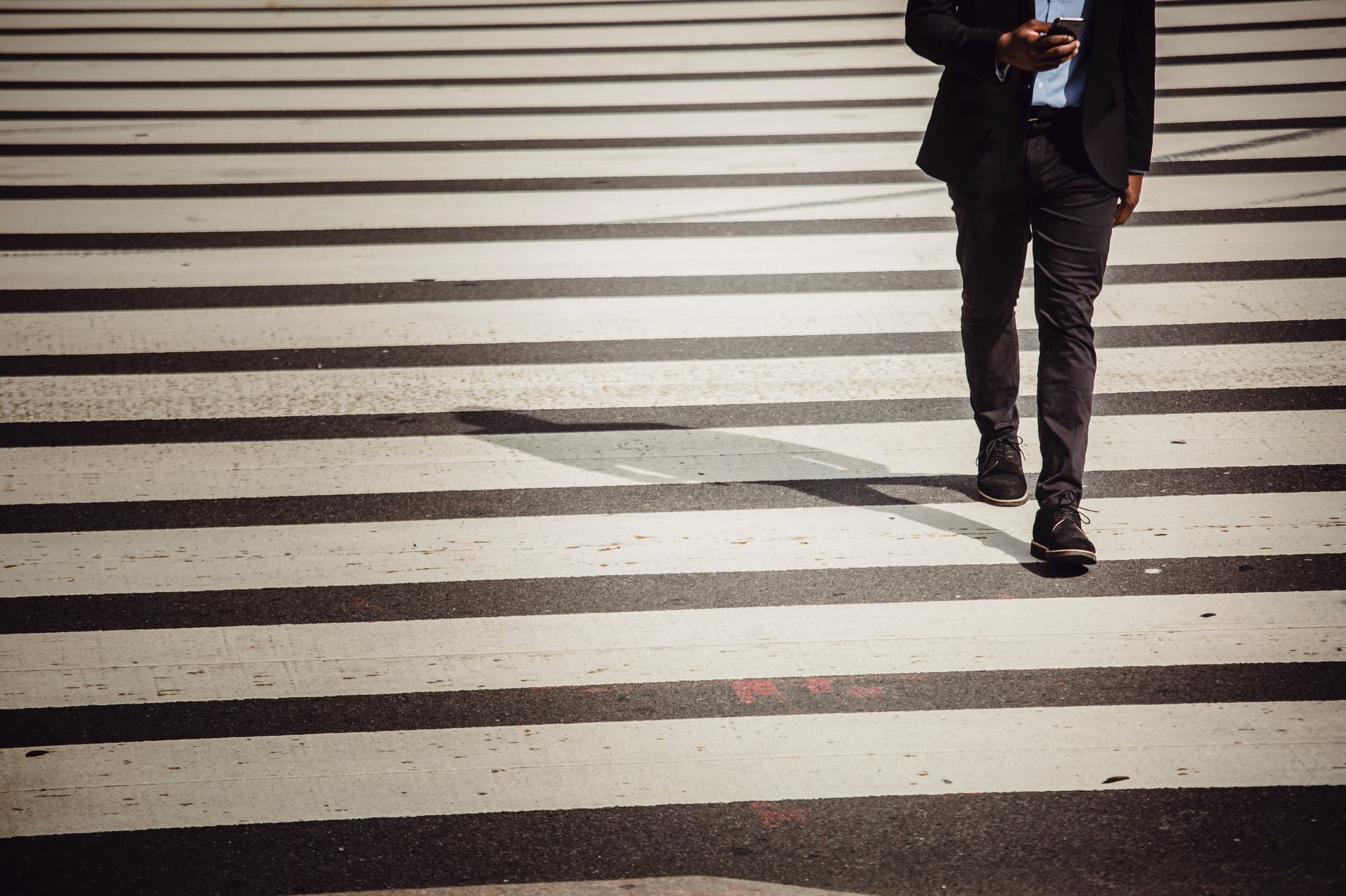 faceless businessman with smartphone walking on crosswalk in sunlight