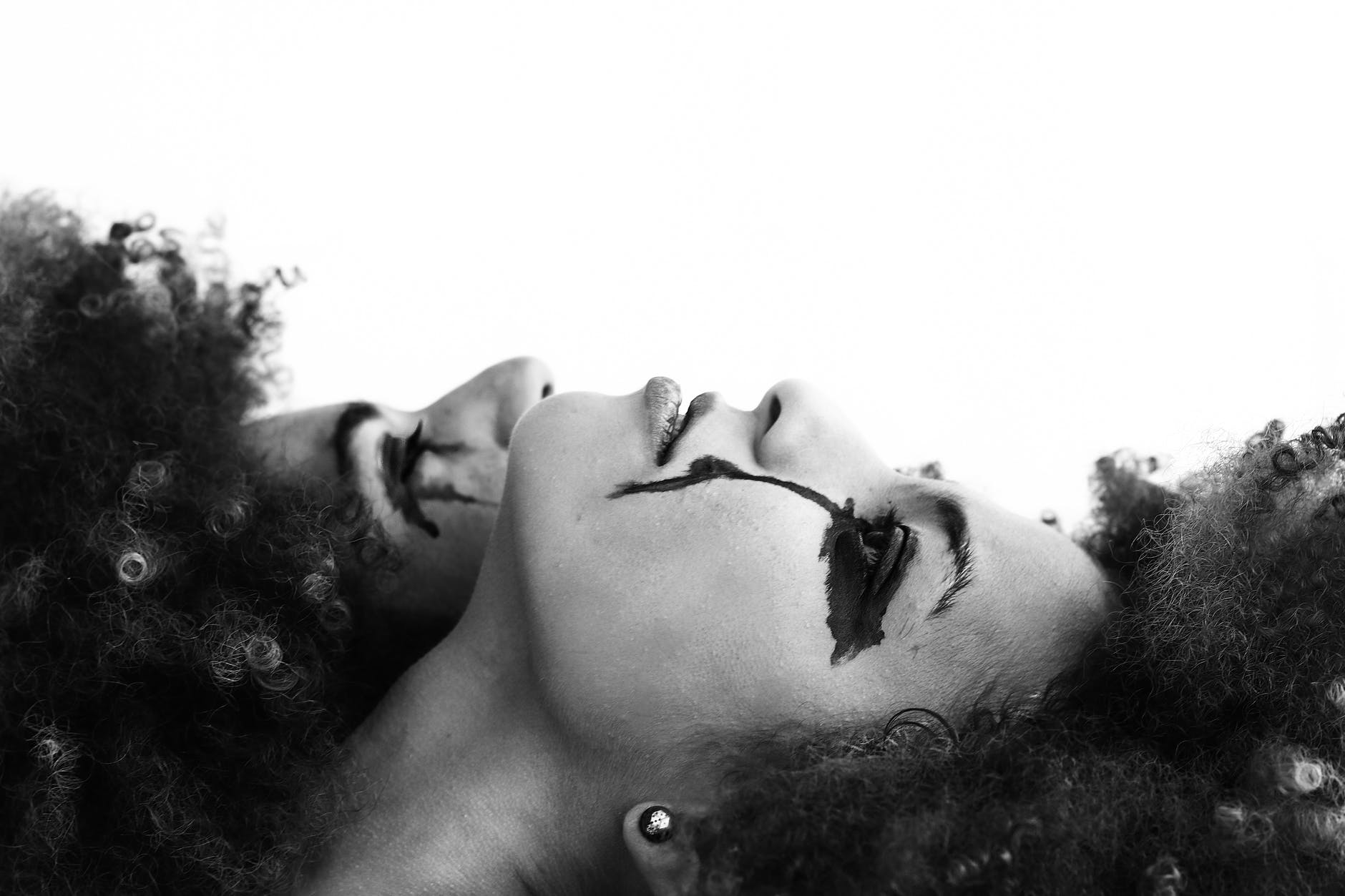 grayscale photo of two women lying on white surface