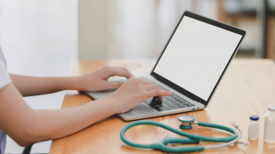 laptop near teal stethoscope in wooden table
