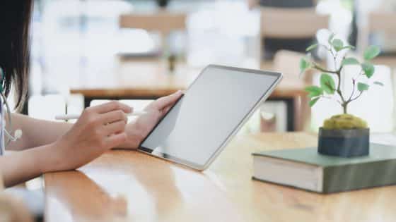 person leaning on wooden table holding white tablet