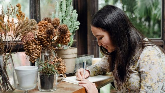 happy young ethnic woman writing article in cozy workplace