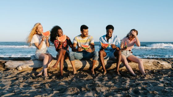 cheerful multiracial friends enjoying watermelon slices on sandy sea shore